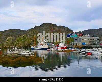 Malerische Küstenlandschaft mit Fischerbooten im Hafen Maniitsoq und farbenfrohen Inuit Häusern an der felsigen Küste vor bewölktem Himmel am frühen Sommermorgen Stockfoto