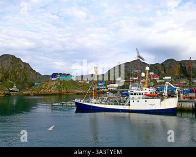Malerischer Blick auf den Fischerhafen Maniitsoq mit Booten und farbenfrohen Inuit-Häusern an der felsigen Küste vor bewölktem Himmel am Frühsommermorgen in Grönland Stockfoto