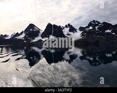 Eine atemberaubende Landschaft mit schneebedeckten Bergen und Gletschern, die sich an einem bewölkten Sommerabend in Wes auf dem ruhigen Wasser des arktischen Eternity Fjords spiegeln Stockfoto