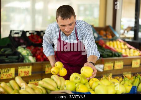 Mann Verkäufer, der im Supermarkt arbeitet und Äpfel auf der Theke verteilt Stockfoto
