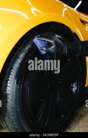 Der Mechaniker wendet ein Produkt mit einem blauen Applikator auf einen schwarzen Reifen an. Schwärzung des Reifenrads des Autos mit Schwamm mit chemischer Schwärzung des Gummis in Stockfoto
