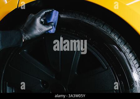 Der Mechaniker wendet ein Produkt mit einem blauen Applikator auf einen schwarzen Reifen an. Schwärzung des Reifenrads des Autos mit Schwamm mit chemischer Schwärzung des Gummis in Stockfoto
