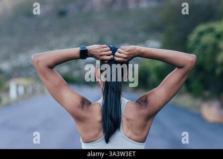 Rückansicht einer schlanken, nicht erkennbaren Frau, die ihr Haar anpasst, während sie im Freien steht Rückansicht einer schlanken, nicht erkennbaren Frau, die ihr Haar anpasst, während St Stockfoto