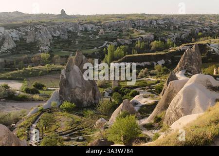 Goldenes Sonnenaufgangslicht über Feenkamine in Goreme, Kappadokien, Türkei. Ein grüner Garten vor den Felsformationen. Ein ganzes Tal darunter Stockfoto