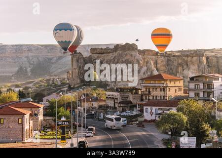 Eine Gruppe farbenfroher Heißluftballons, die bei Sonnenaufgang in der Nähe der felsigen Landschaften von Goreme, Kappadokien, Türkei, schweben. Eine Stadt im Vordergrund. Stockfoto