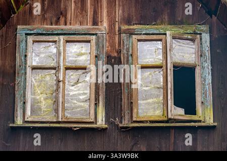 Ein paar beschädigte Fenster an der Fassade eines alten Holzhauses Stockfoto