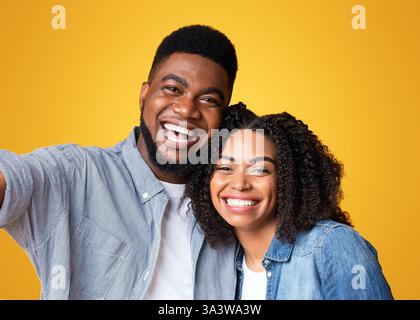 Ein fröhliches Paar teilt einen fröhlichen Moment vor einem hellgelben Hintergrund Stockfoto