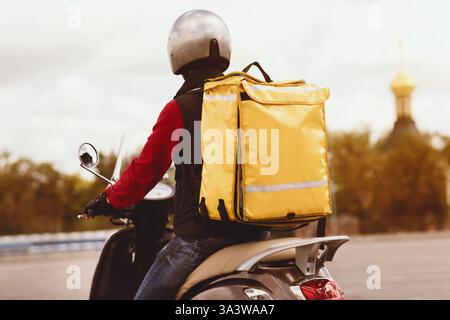 Kurier Mit Gelbem Rucksack, Der Mahlzeiten Auf Dem Roller Draußen Serviert, Rückansicht Stockfoto