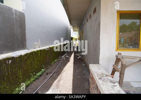 Eine enge Gasse zwischen zwei Gebäuden mit unvollendeten bemalten Wänden. Eine Seite hat moosbedeckte Wände, während der Boden mit verstreuten d unbefestigt bleibt Stockfoto