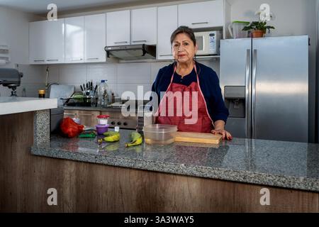 Ältere hispanische Frau, die Schürze trägt, in der Küche steht und Zutaten für das Kochen vorbereitet Stockfoto