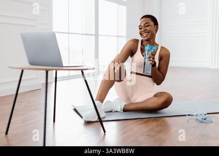 Junge afroamerikanische Frau genießt gesundes Getränk nach dem Heimtraining Stockfoto