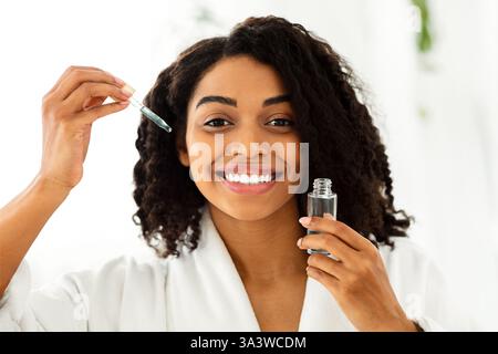 Hautpflegeprodukte. Lächelnde Afrikanische Frau Holding Flasche Mit Feuchtigkeitsspendenden Gesicht Serum Stockfoto