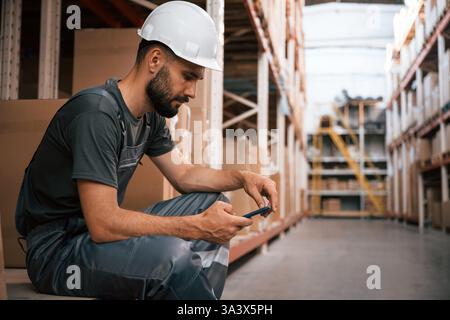 Eine Pause machen, mit dem Smartphone sitzen. Foreman ist im Lager, im Versandhandel. Stockfoto