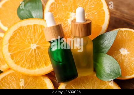 Flaschen mit ätherischem Orangenöl und geschnittenem frischem Obst auf hölzernem Hintergrund, Nahaufnahme Stockfoto