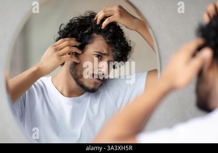 Behandlung der Haarpflege. Besorgt indischen Kerl Blick auf schuppige Kopfhaut im Spiegel, Untersuchung graues Haar und Haarausfall Problem Stockfoto