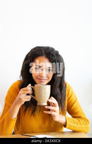 Junge lateinfrau, die ein warmes Getränk in einem gemütlichen Café genießt Stockfoto