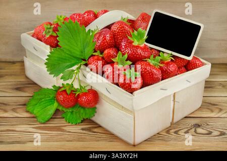Erdbeeren und Etikett in einem Korb auf hölzernem Hintergrund Stockfoto