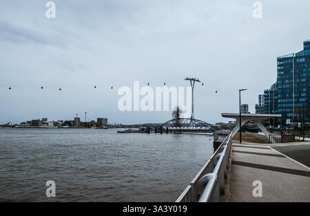 Ein Blick vom Ufer der Themse in der Nähe des North Greenwich Pier und der Londoner Cable Car-Linie an einem langweiligen, bewölkten Tag im Spätwinter Stockfoto