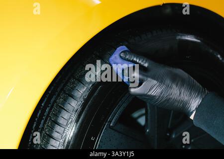 Schwärzung des Reifenrads des Autos mit Schwamm mit chemischer Schwärzung des Gummis bei der Detaillierung des Autoservice. Der Mechaniker wendet ein Produkt auf einen schwarzen Reifen an Stockfoto