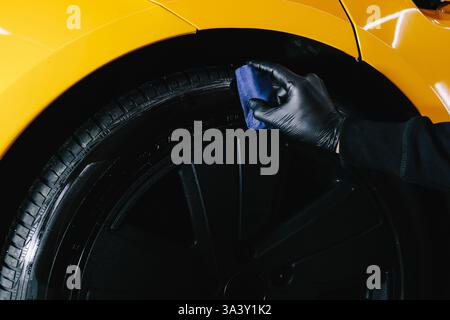 Schwärzung des Reifenrads des Autos mit Schwamm mit chemischer Schwärzung des Gummis bei der Detaillierung des Autoservice. Der Mechaniker wendet ein Produkt auf einen schwarzen Reifen an Stockfoto