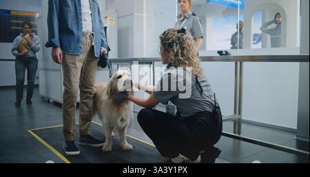 Reifer Mann mit Haustier während des Screening-Verfahrens im Flughafenterminal: Weibliche TSA-Beamtin scannt Golden Retriever Dog mit Metalldetektor. Tierinspektion am Sicherheitskontrollpunkt für das Einsteigen in den Flug. Stockfoto
