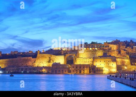 Historische befestigte Stadt Valletta, Malta, beleuchtet in der Abenddämmerung von der Uferpromenade des Grand Harbour. Stockfoto