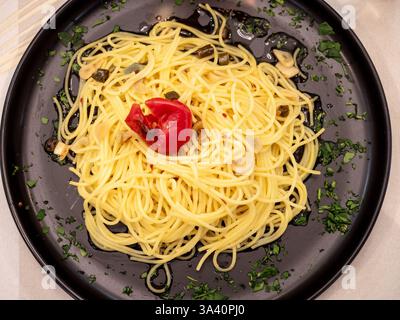 Spaghetti mit Knoblauch, Öl, Chili und Petersilie auf einem schwarzen Teller serviert, garniert mit gehackter Petersilie und getrockneter Tomate, ein Klassiker von mir Stockfoto