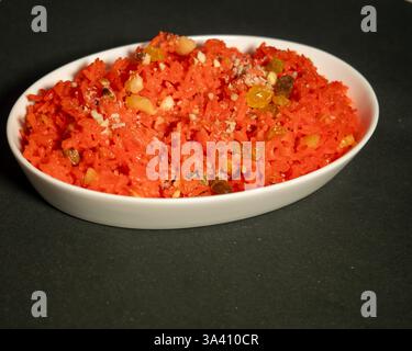 Gajar ka Halwa, ein traditionelles indisches süßes Dessert aus geriebenen Karotten, Milch, Zucker, Nüssen und Gewürzen, serviert auf einem eleganten weißen ovalen Teller, cre Stockfoto