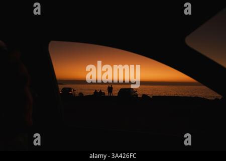 Sonnenuntergang und Reisen, ein Paar, das den Sonnenschein mit anderen Leuten im Auto beobachtet, Aussichtspunkt von einem Passagier mit offenem Fenster, Blick auf das Meer. Stockfoto