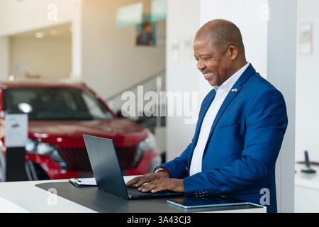 Glücklicher afroamerikanischer Kunde, der den Kauf eines Fahrzeugs in einem belebten Verkaufsraum eines Händlers beendet Stockfoto