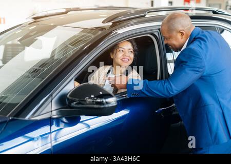 Junge afroamerikanische Frau, die bei einem Fahrzeugkauf in einem Händlerbetrieb mit einem Autohändler interagiert Stockfoto