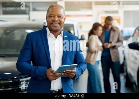 Glückliches Paar, das seinen Autokauf in einem Händlerbetrieb beendet, und ein lächelnder Verkäufer hilft ihm Stockfoto