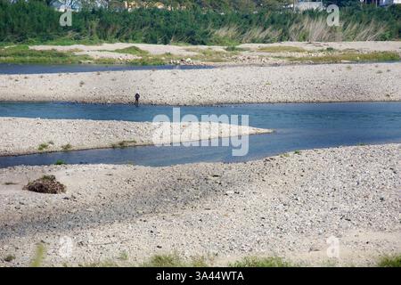 Gwangyang City, Südkorea - 3. Oktober 2021: Ein einsamer Fischer steht auf einer felsigen Sandbank im Seomjingang River und wirft seine Schnur in die seichte Tiefe Stockfoto