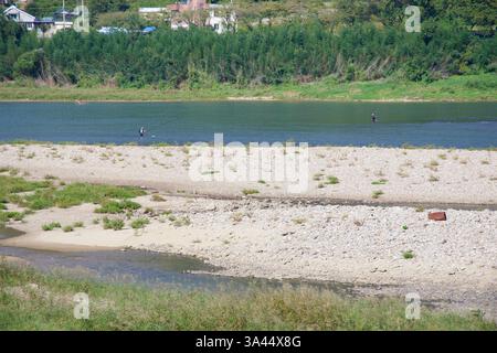 Gwangyang City, Südkorea - 3. Oktober 2021: Zwei Fischer waten im Seomjingang River und werfen ihre Linien in das fließende Wasser, umgeben von Stockfoto