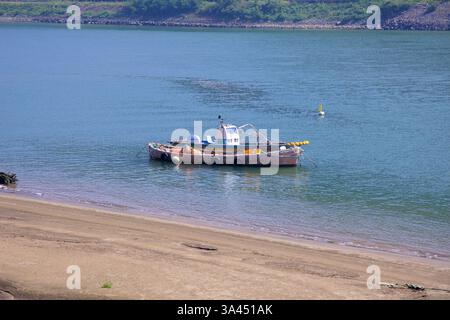 Gwangyang City, Südkorea - 3. Oktober 2021: Ein verwittertes Fischerboot schwimmt auf den ruhigen Gewässern des Seomjin River nahe einer Sandküste. Die sce Stockfoto
