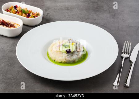 Gourmet-Garnelen- und Weißfisch-Tartar mit Avocadomousse, essbaren Blumen und grüner Sauce, serviert auf einem weißen Teller Stockfoto
