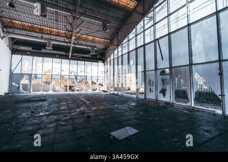 Das Innere des verlassenen Industriebaus wurde für den Abriss vorbereitet mit kaputten Fenstern, zersplittertem Glas, beschädigter Decke, Schutt auf schmutzigem Boden, Vandalen Stockfoto