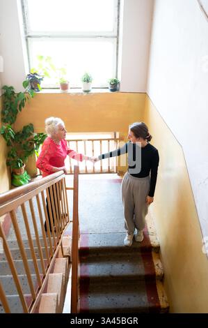 Zwei Frauen, eine ältere und eine junge, teilen einen Moment von Herzen, während sie auf der Treppe stehen. Das warme Licht unterstreicht ihre Verbindung, umgeben von ihnen Stockfoto