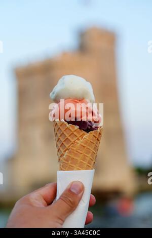 Hand hält eine Eiskegel mit drei köstlichen Schaufeln vor einem historischen Gebäude Stockfoto