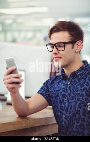 Junger Mann in Brille, der im Büro Smartphone benutzt und sich auf den Bildschirm konzentriert Stockfoto