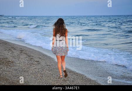 Das Foto zeigt eine junge Frau, die entlang eines Kieselstrandes am Rand der Brandung läuft. Stockfoto