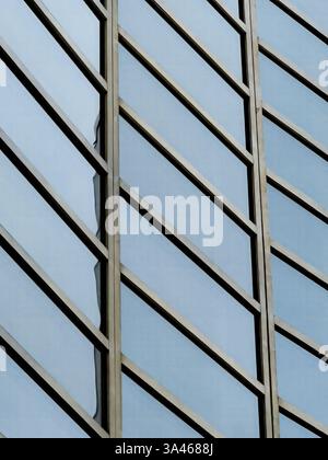 Eine markante Glas- und Metallfassade mit diagonalen Linien und blauen Reflexen, die moderne Architektur, geometrisches Design und städtische Ästhetik präsentiert. Stockfoto