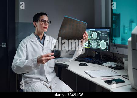 Wissenschaftler im Laborkittel zur Untersuchung eines Röntgenbildes in einem medizinischen Labor. Computerbildschirm, der medizinische Scans im Hintergrund anzeigt, Laborumgebung offensichtlich Stockfoto