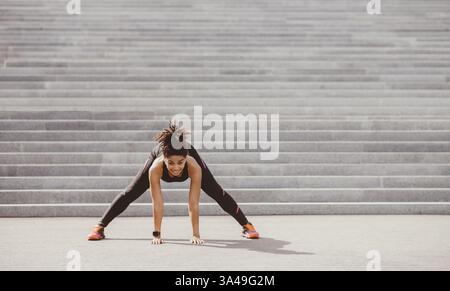 Übungen für Flexibilität. Fröhliche afroamerikanische Mädchen in Sportswear mit Fitness-Tracker tun Stretching Stockfoto