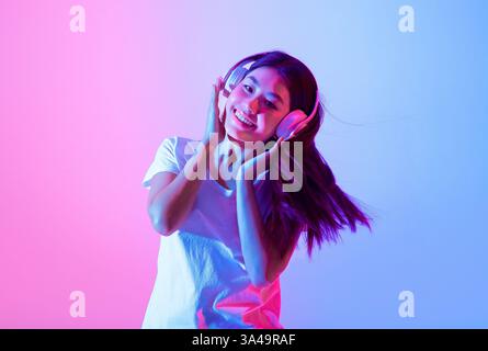 Glückliche junge Frau, die Musik mit Kopfhörern in farbenfroher Beleuchtung genießt Stockfoto