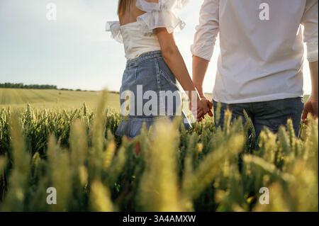Halten sich gegenseitig die Hände. Ein nettes Paar ist zusammen auf dem grünen Ackerfeld. Stockfoto