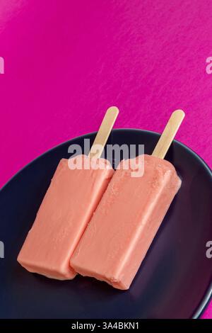 Eis von schwarzen Beeren, die auf blauem Schälchen und Fuchsia-Hintergrund schmelzen. Leerzeichen Stockfoto
