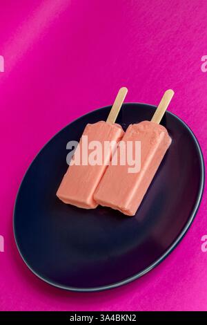 Eis von schwarzen Beeren, die auf blauem Schälchen und Fuchsia-Hintergrund schmelzen. Leerzeichen Stockfoto