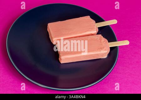 Eis von schwarzen Beeren, die auf blauem Schälchen und Fuchsia-Hintergrund schmelzen. Stockfoto