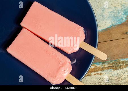 Eis aus roten Beeren, die auf blauem Gericht und farbenfrohem Hintergrund schmelzen. Stockfoto